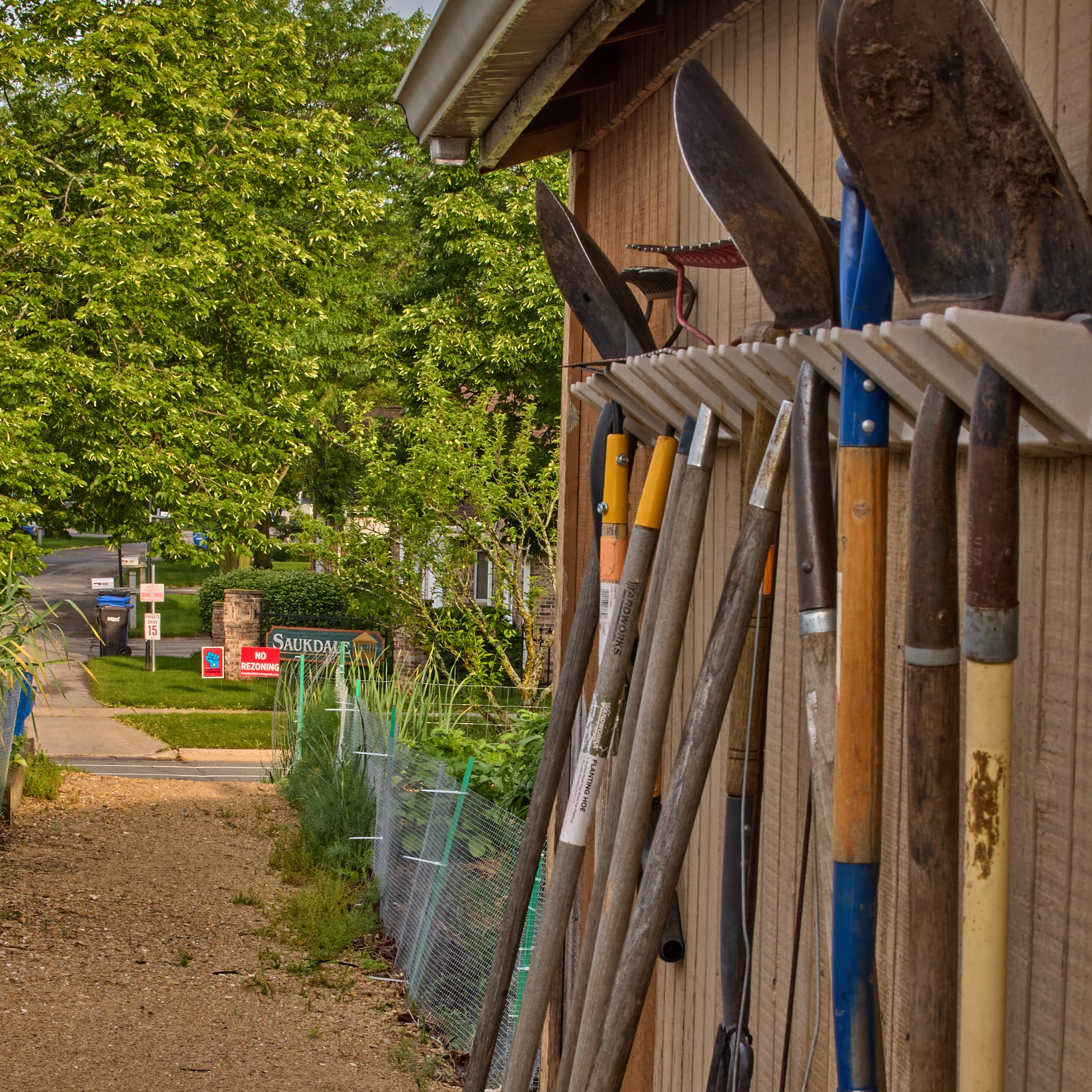 Photograph of gardening tools hanging outside a shed.